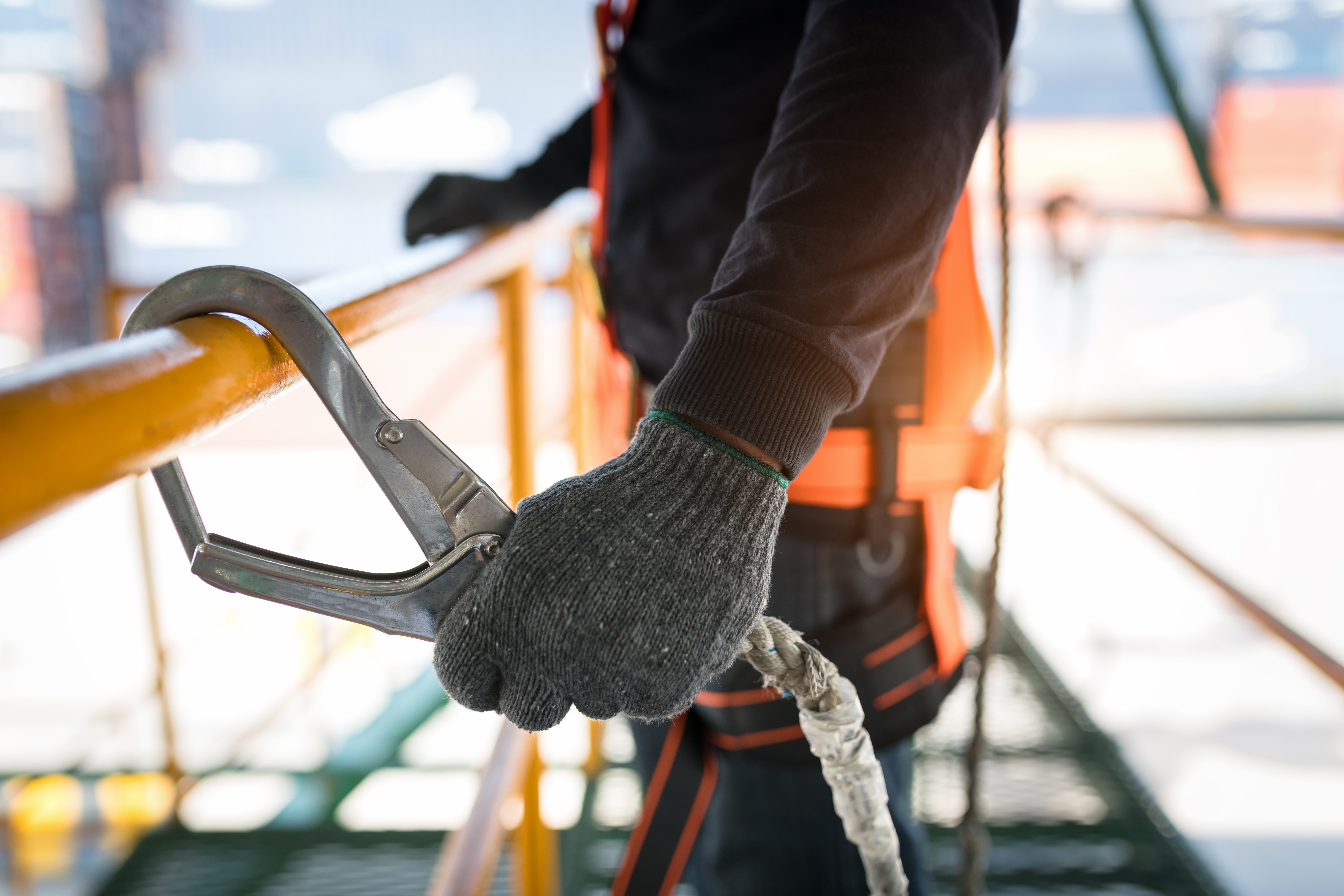 Trabalhador utilizando equipamento de segurança com corda e mosquetão em andaime, representando segurança e eficiência na construção civil.