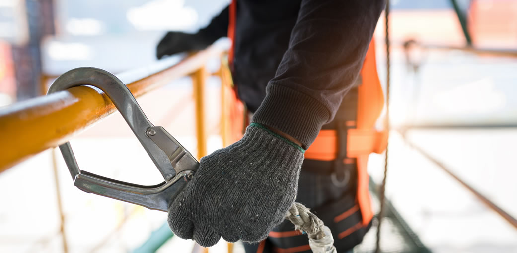 Trabalhador utilizando equipamento de segurança com corda e mosquetão em andaime, representando segurança e eficiência na construção civil.